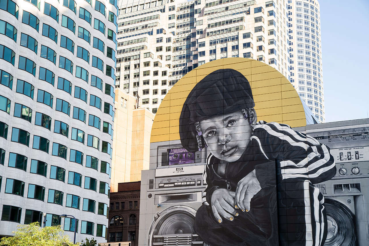 This mural features a young girl, Rob Gibbs' daughter, in a track suit and crouching in front of a boom box, with the skyline as a backdrop.