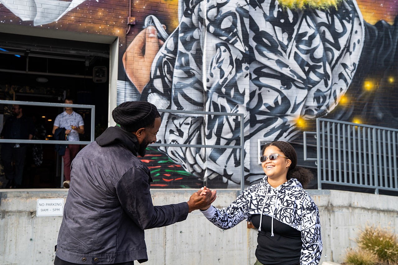 Bobby Boyd, in a black jacket and beanie, and Power Mission Walker Augustin, in a white sweatshirt with black markings, smile and dap up each other.