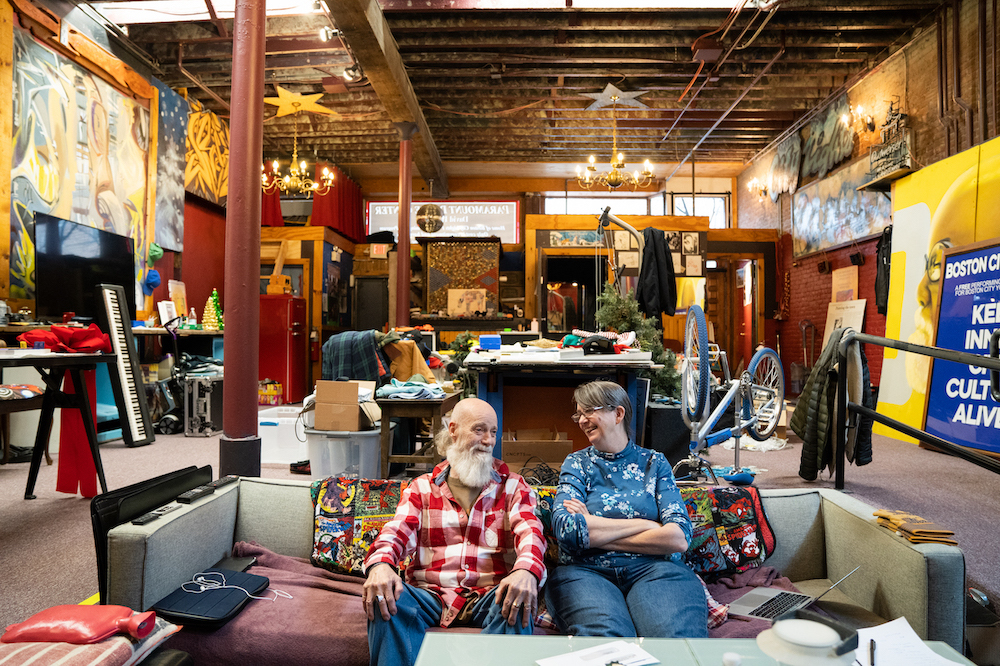 Duggan Hill and Tiane Donahue sitting inside Boston City Lights Performing Arts School, surrounded by artwork.