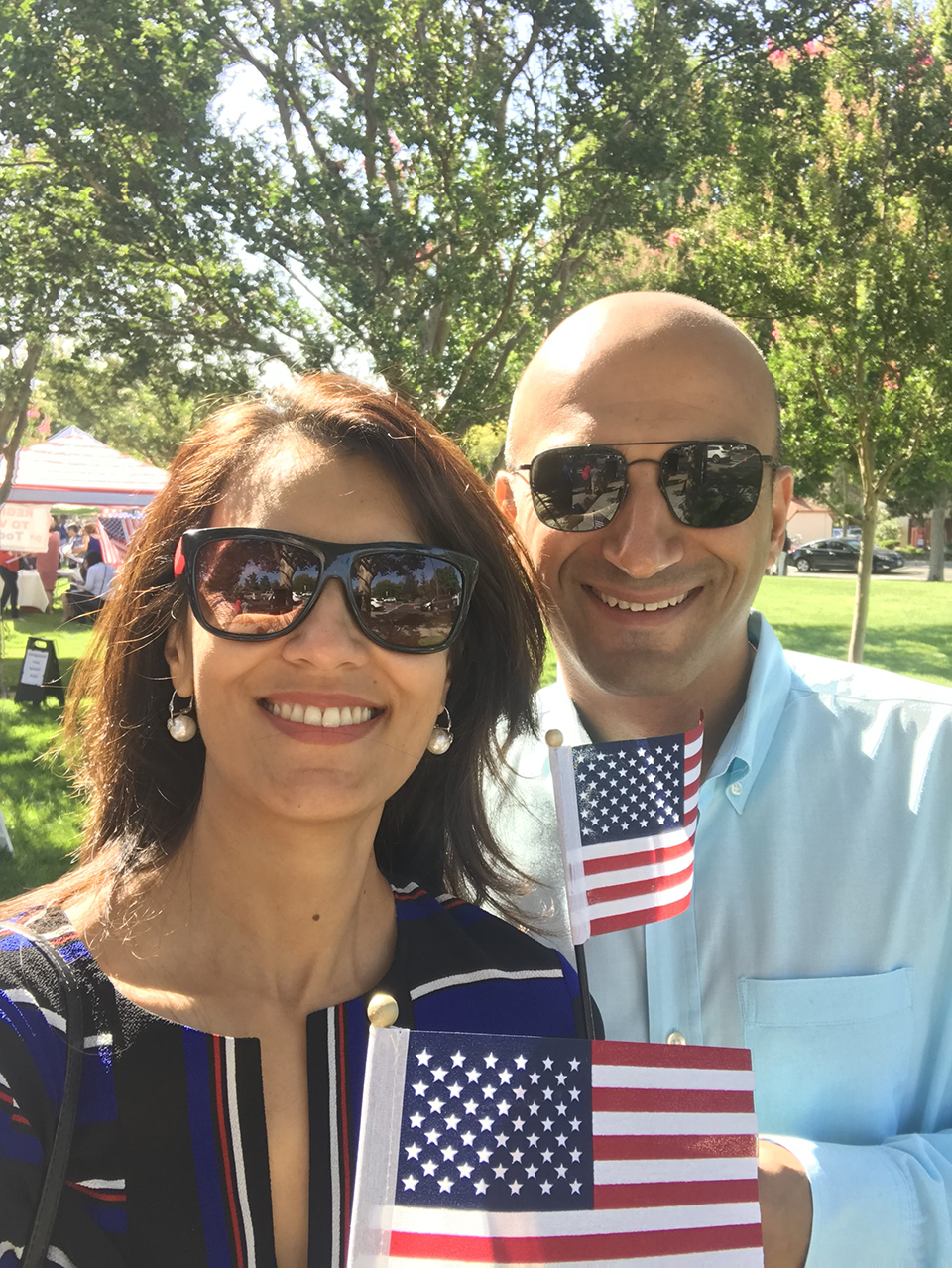 A man and a woman take a photo outside while holding American flags.