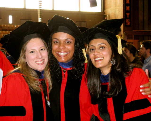 Three women wearing red and black graduation regalia pose for a photo together.