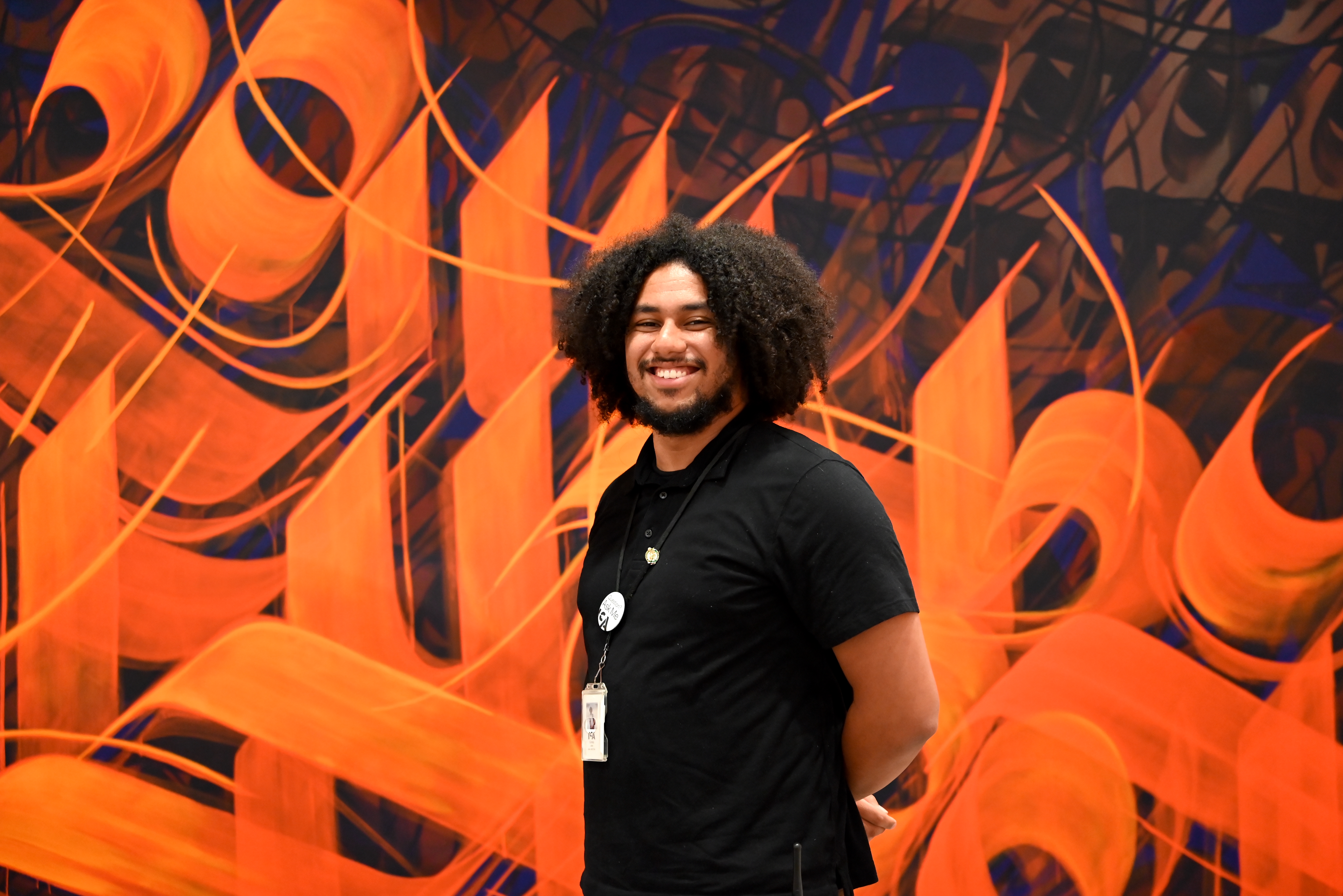 A smiling museum staff member stands in front of a large orange abstract mural.