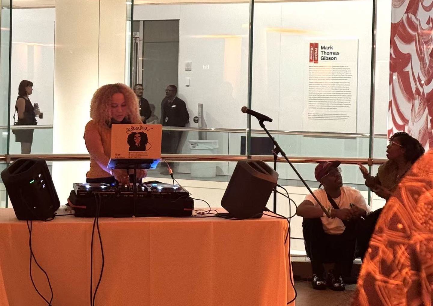 A female DJ performs inside a museum during a nighttime event, with visitors gathered nearby.